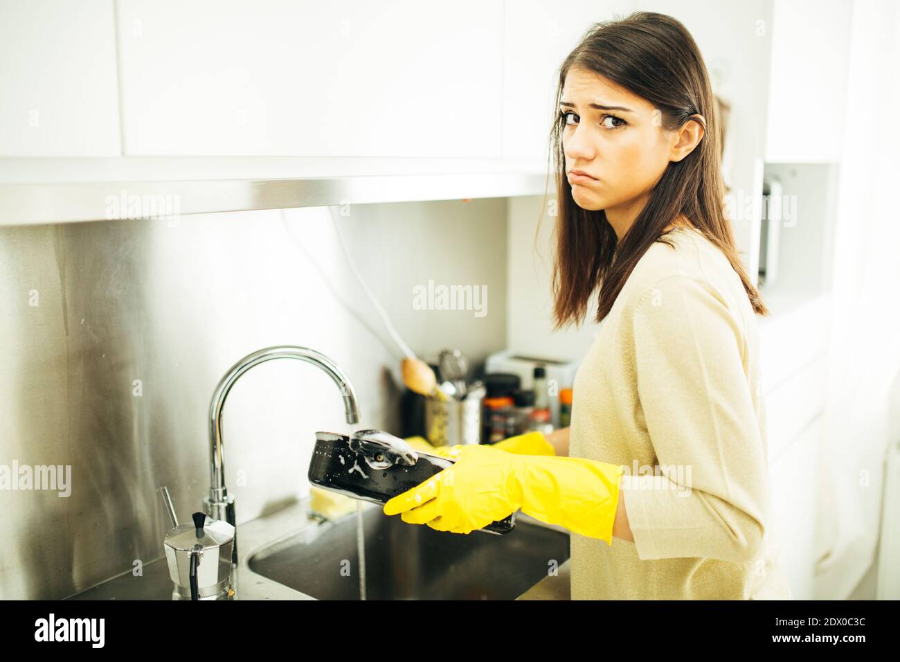 Donna stanca di lavarsi a mano e di pulizia chores.Housewife donna lavare piatti in cucina. Lavare le piastre manualmente, indossando la gomma gialla di pulizia glo Foto Stock