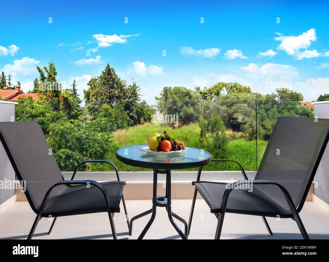Vista frontale del balcone aperto con vista sul giardino estivo nella foresta di campagna. Terrazza patio con tavolo di vetro, sedie e frutta piatto Foto Stock