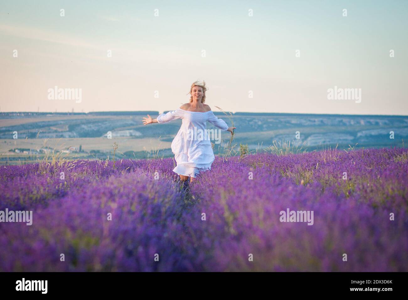 Bella donna in abito bianco corre in un campo di lavanda Foto Stock