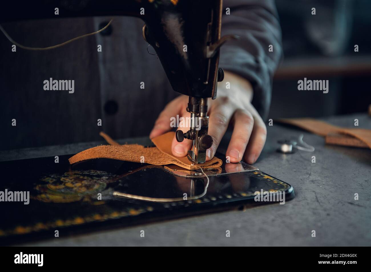 Primo piano di una cucitura filare di alta qualità su un pezzo di vera pelle marrone. Mani di un sarto e di una macchina da cucire. Foto Stock