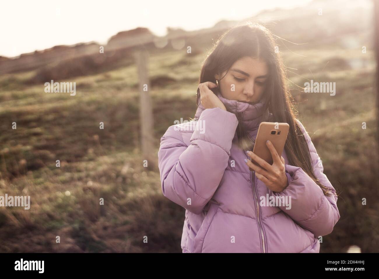 Giovane donna latina con porpora che scrive un messaggio con il suo smartphone visto attraverso la finestra di un'auto, nella collina in Cantabria, nel nord della Spagna Foto Stock