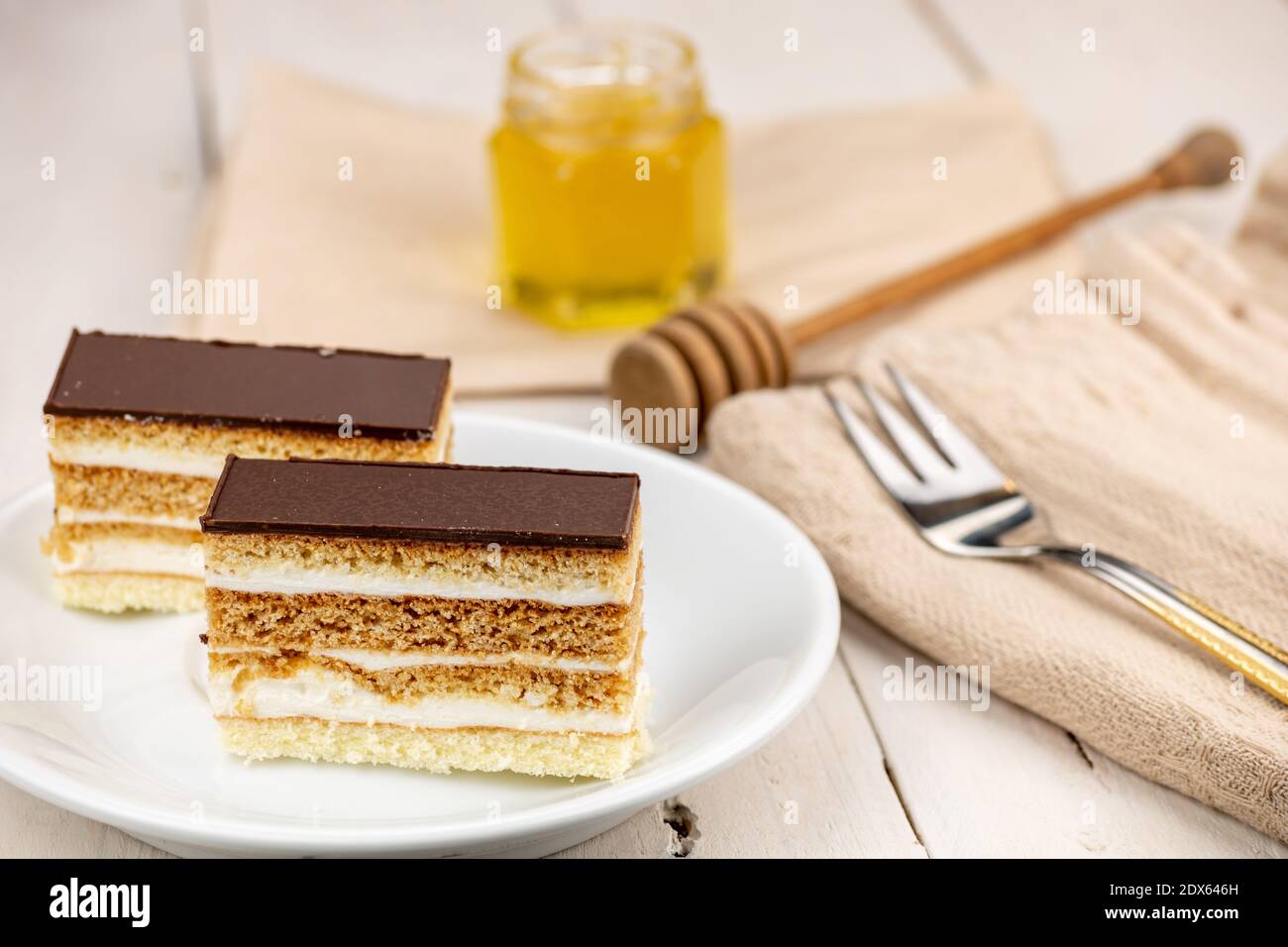 Torta al miele con guarnizione al cioccolato e crema al burro bianco. Dolce di nozze fatto in casa. Servito su un tavolo di legno bianco. Miele in vetro come decorazione. Foto Stock