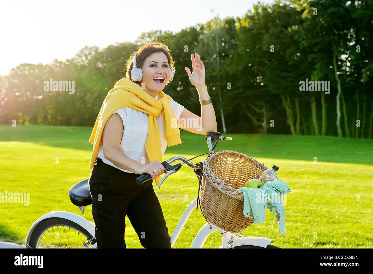 Bella donna di mezza età felice in cuffia con bicicletta nel parco Foto Stock