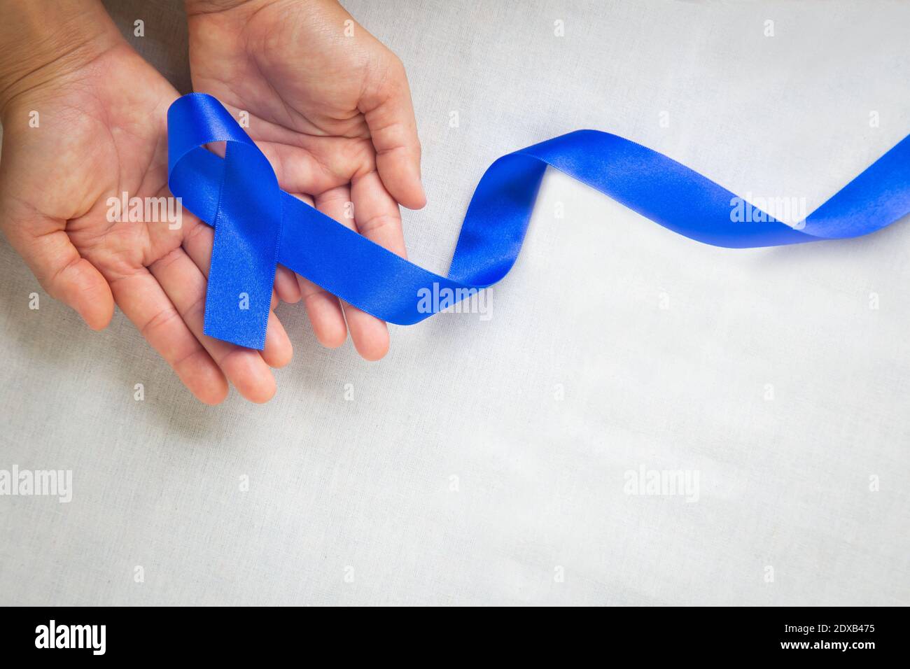 Mani che tengono il nastro blu profondo su tessuto bianco con spazio per la copia. Consapevolezza del cancro colorettale, cancro del colon della persona anziana e giornata mondiale del diabete, Chil Foto Stock