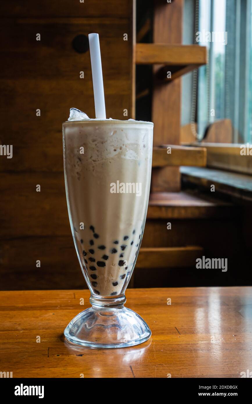 Primo piano della tradizionale bevanda a base di tè al latte a bolle taiwanese, bevanda fredda taiwanese su classico tavolo in legno. Foto Stock