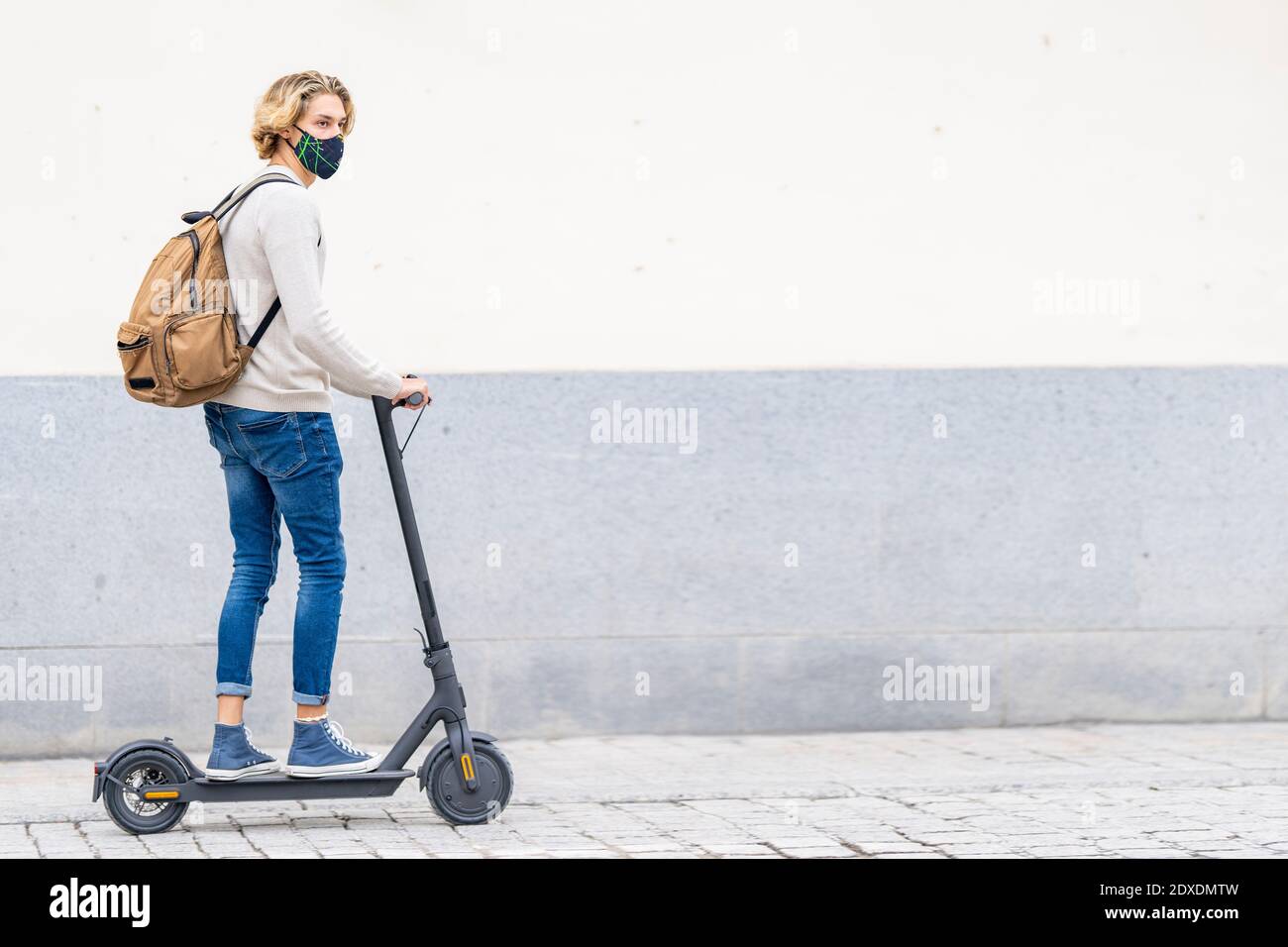 Uomo con maschera facciale e zaino guidando scooter elettrico a spinta sul sentiero Foto Stock