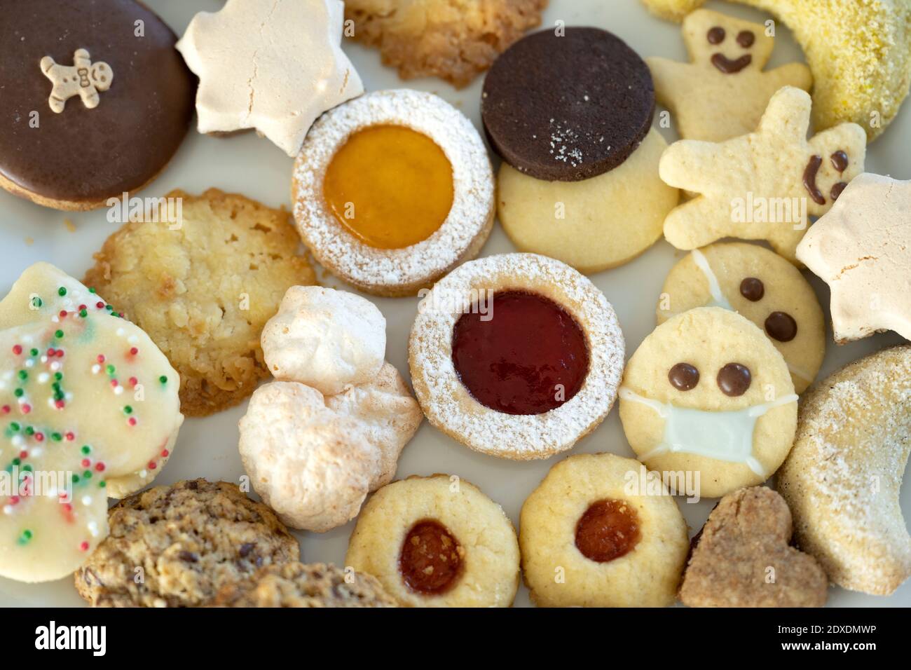 Vari biscotti di Natale pronti da mangiare, uno che indossa una maschera protettiva per il viso Foto Stock