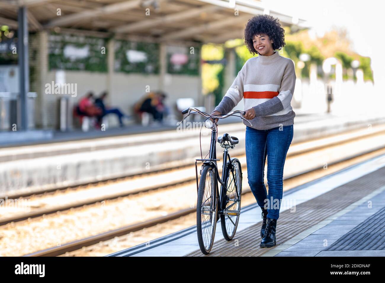 Giovane donna che cammina con la bicicletta mentre il giorno sogna alla ferrovia piattaforma della stazione Foto Stock