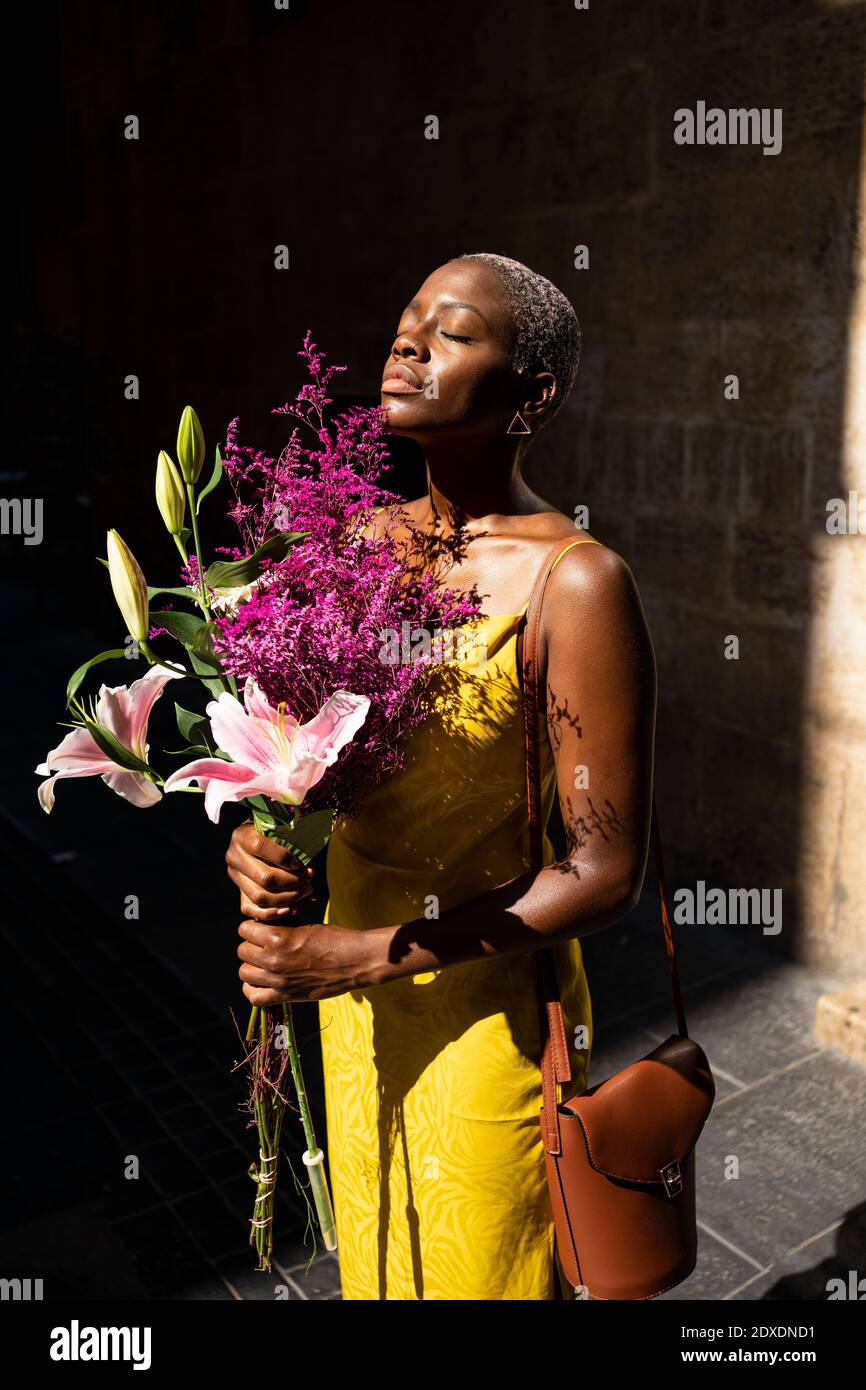 Donna mid adulta con gli occhi chiusi tenendo il bouquet di fiori sopra giorno di sole Foto Stock