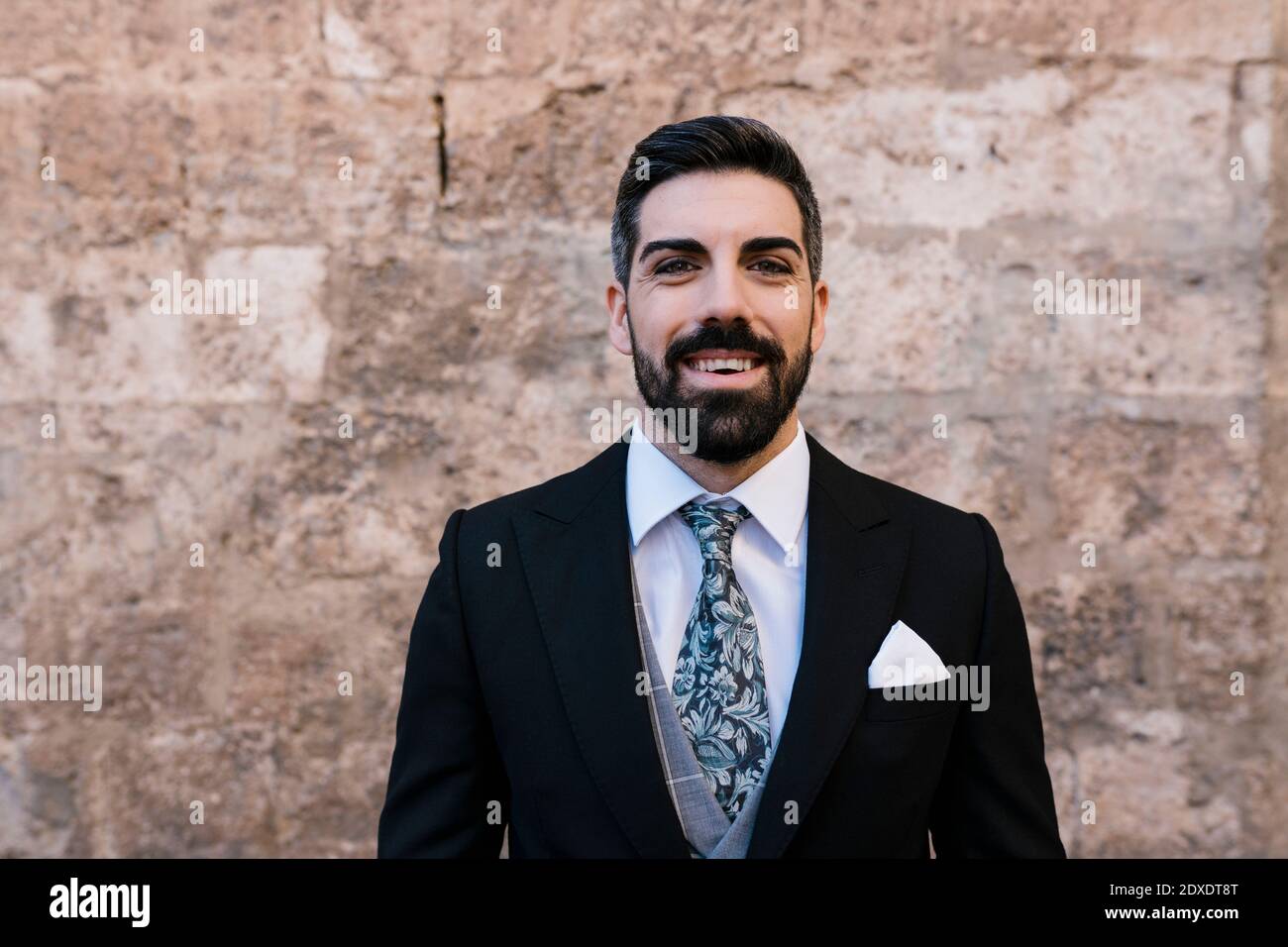 Buon sposo con costume e cravatta contro il muro Foto Stock