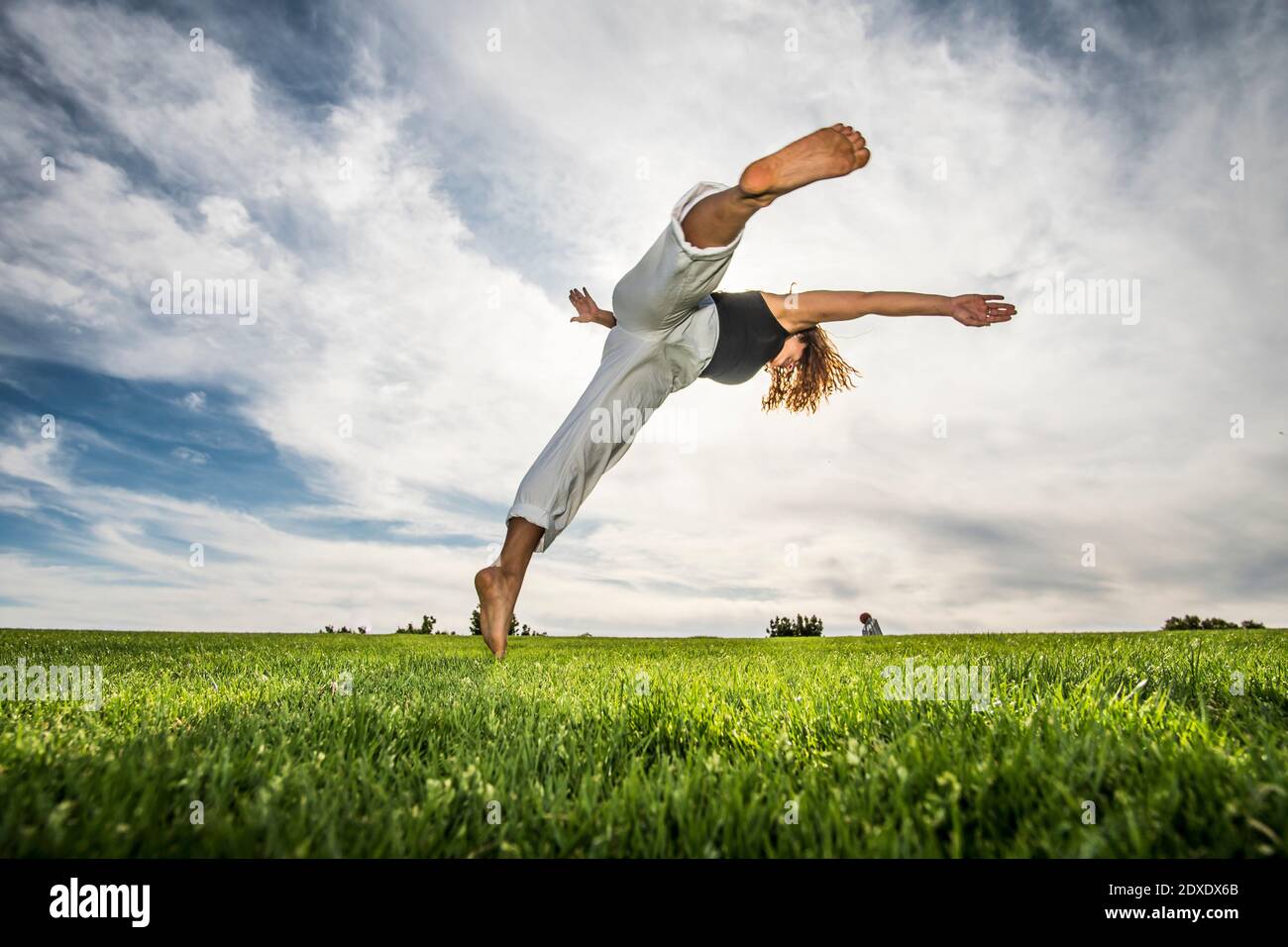 acrobata femmina che fa movimento in parco contro cielo nuvoloso Foto Stock