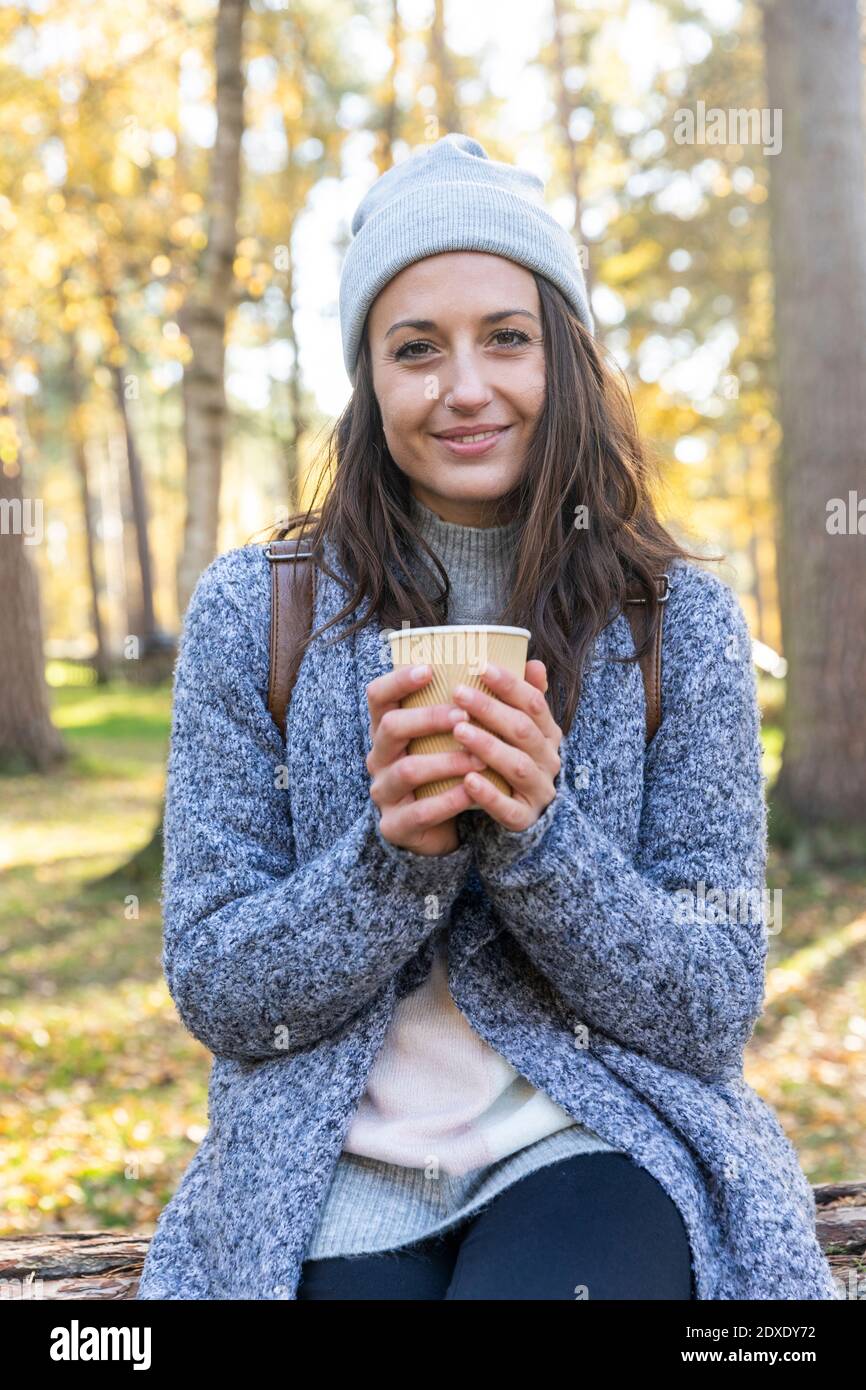 Sorridente escursionista femminile che tiene una tazza da tè nel bosco di Cannock Chase durante l'inverno Foto Stock