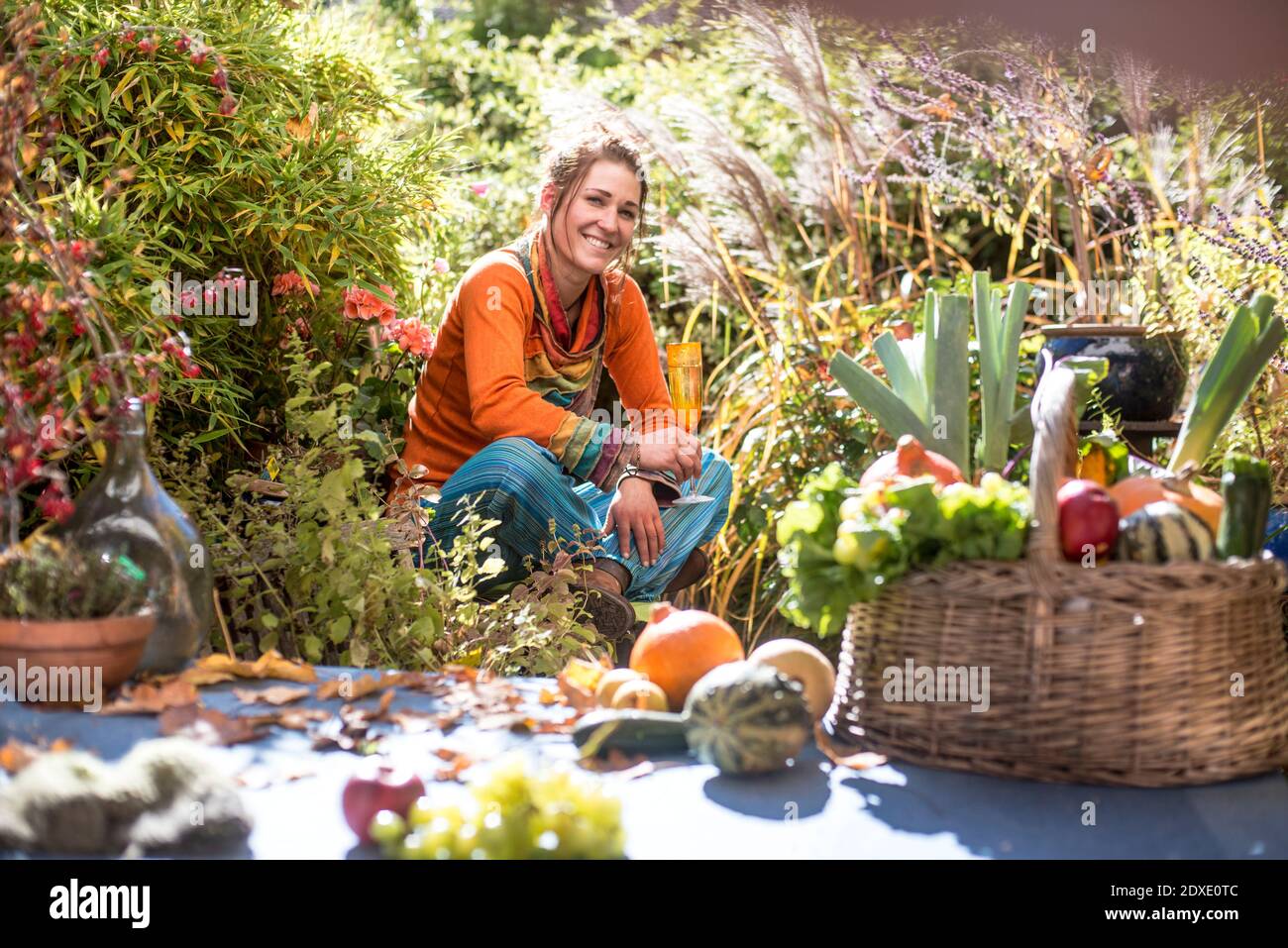 Donna sorridente che raccoglie frutta e verdura mentre si siede in giardino Foto Stock