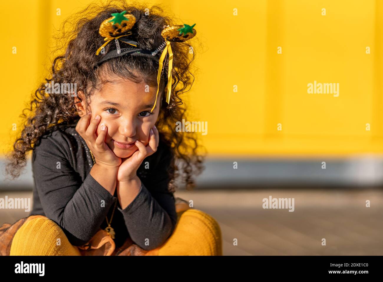 Ragazza seduta con la testa in mani contro il muro giallo Foto Stock