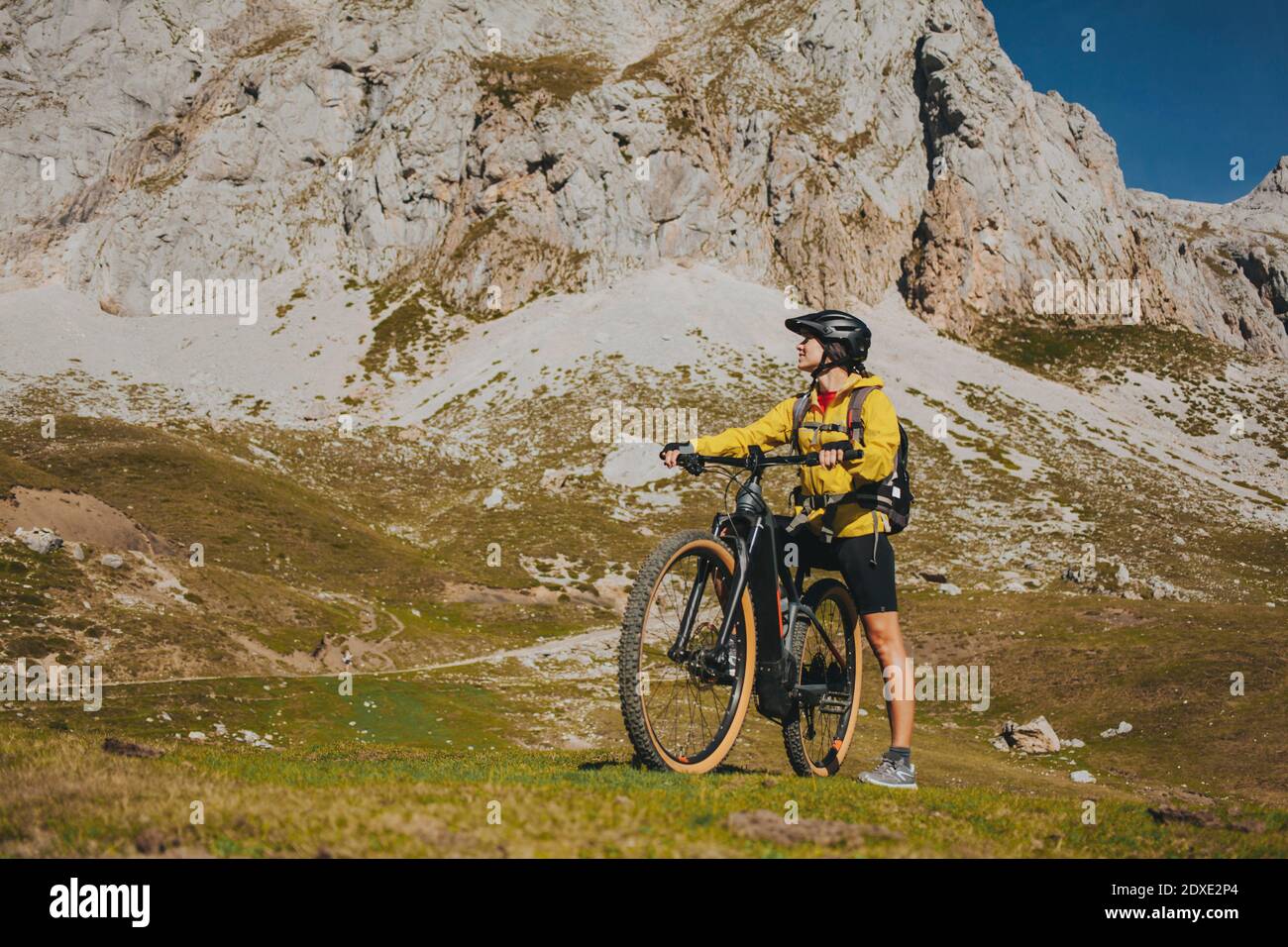 Donna con bicicletta che guarda lontano contro la montagna rocciosa in giornata di sole, Parco Nazionale Picos de Europa, Cantabria, Spagna Foto Stock