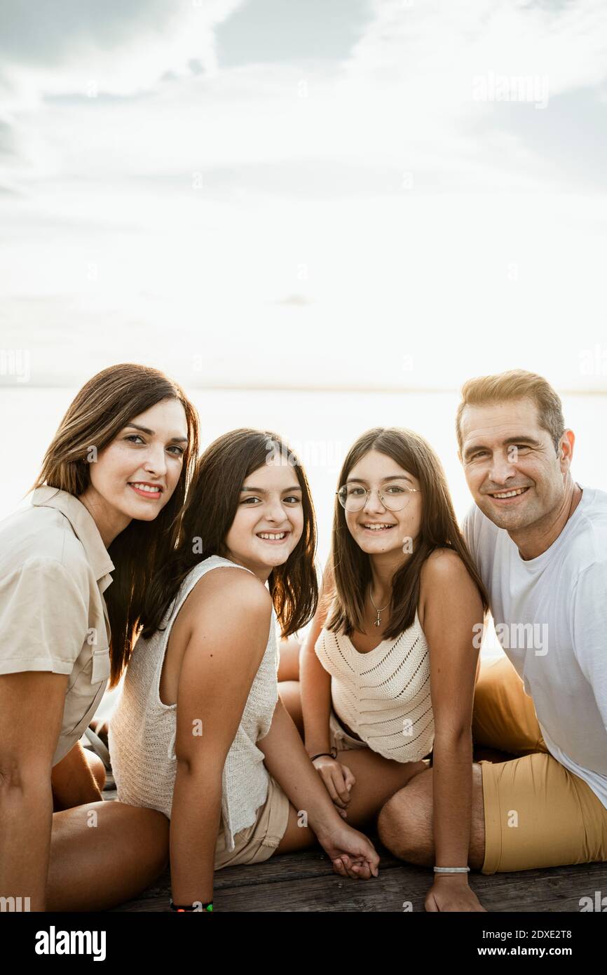 Famiglia sorridente seduta sul molo contro il cielo Foto Stock