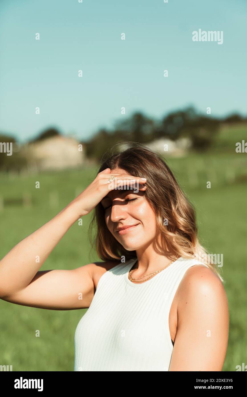 Giovane donna che scherma gli occhi con la mano in parcheggio durante estate Foto Stock