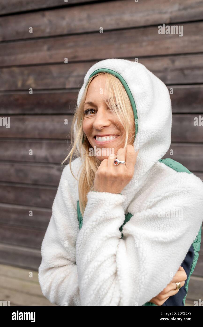 Donna sorridente in abiti da cappuccio in piedi contro il muro di legno Foto Stock