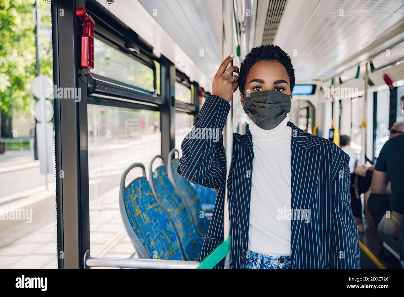 Donna d'affari in piedi appoggiandosi sul palo in autobus durante COVID-19 Foto Stock