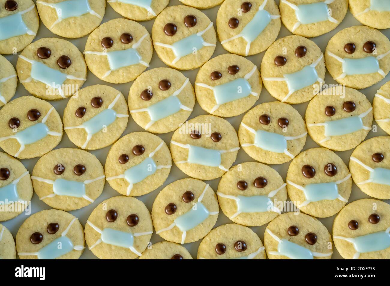 File di biscotti natalizi con volti che indossano maschere facciali di protezione Foto Stock