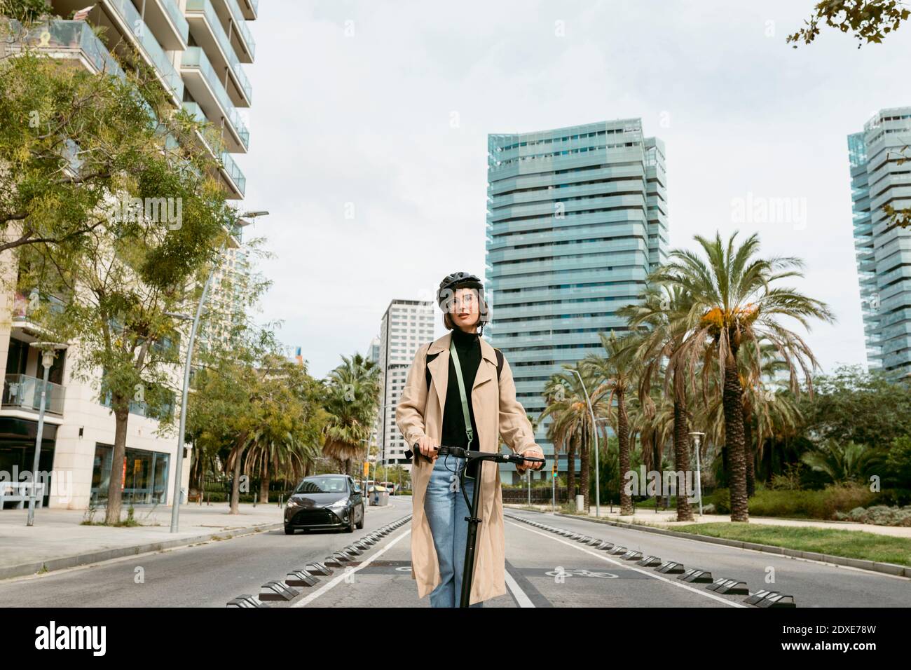 Donna mid adulta che guida scooter elettrico a spinta in città Foto Stock