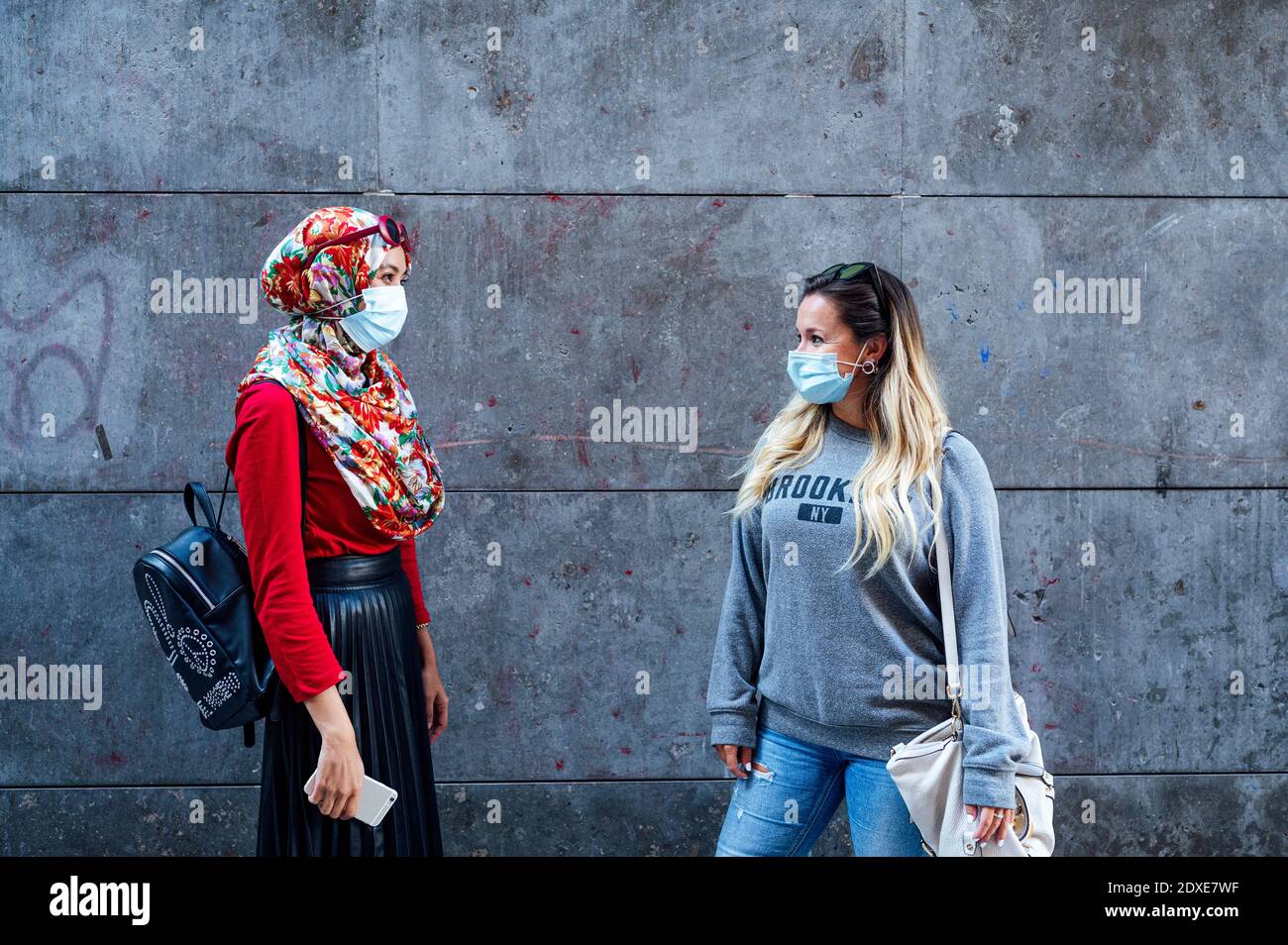 Amici femminili che si guardano l'un l'altro mentre si levano in piedi contro il grigio Muro durante COVID-19 Foto Stock