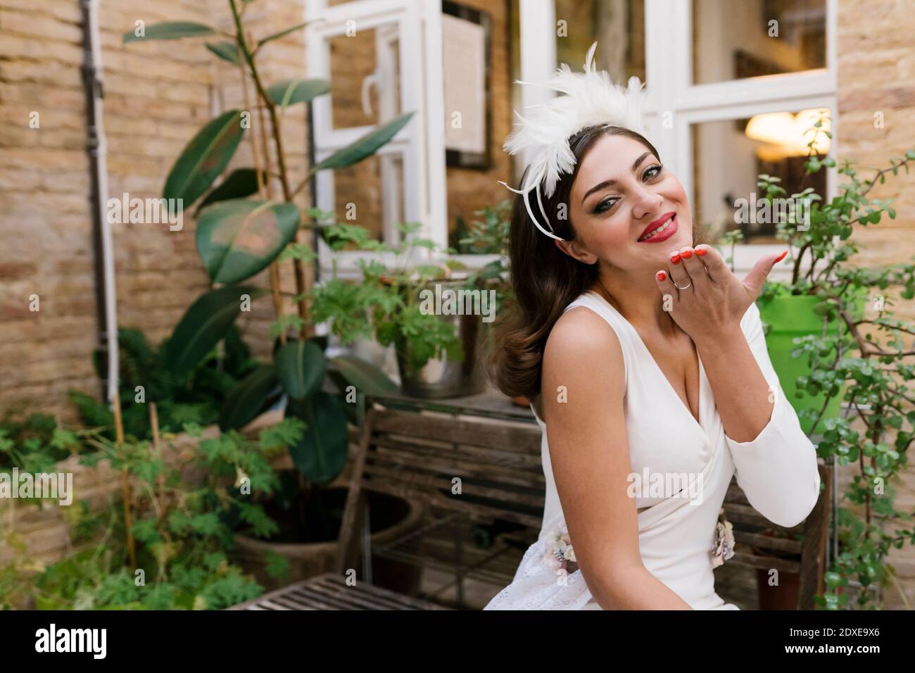 Sposa sorridente che dà bacio volante mentre si siede in giardino contro piante Foto Stock