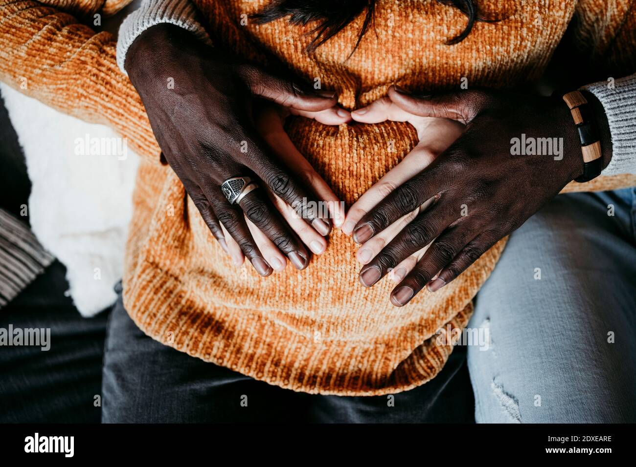 L'uomo e la donna incinta formano la forma del cuore con le mani sopra pancia a casa Foto Stock
