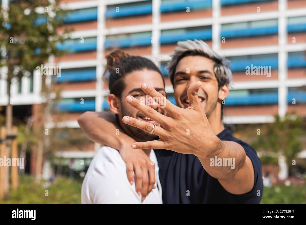 Uomo sorridente che mostra un anello di fidanzamento mentre si è in piedi  da un partner gay nel parco Foto stock - Alamy