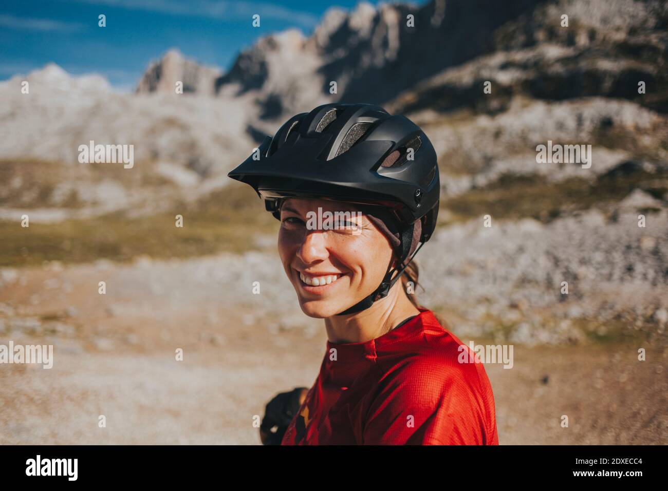Donna sorridente che indossa un casco da ciclismo il giorno di sole, Parco Nazionale Picos de Europa, Cantabria, Spagna Foto Stock