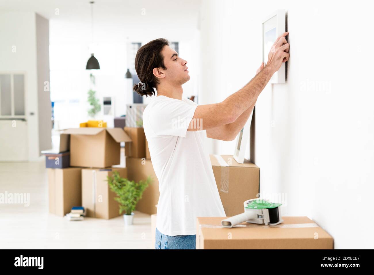 Giovane uomo che mette in su la cornice dell'immagine sulla parete alla sua nuovo appartamento Foto Stock