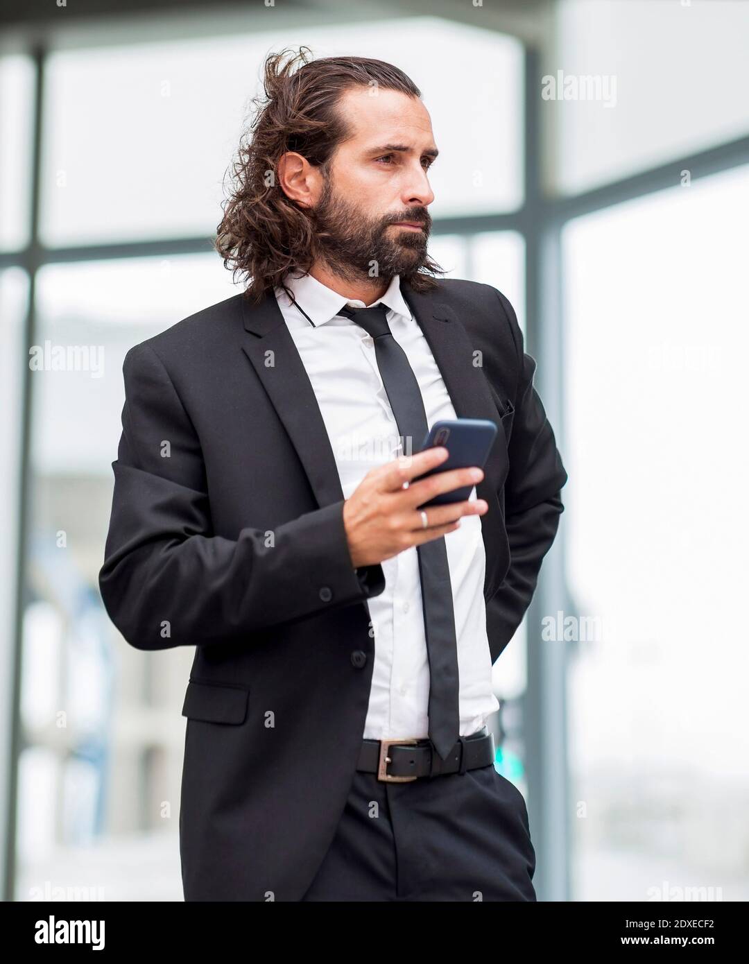 Ritratto di uomo d'affari in piedi indoor con smartphone in mano Foto Stock