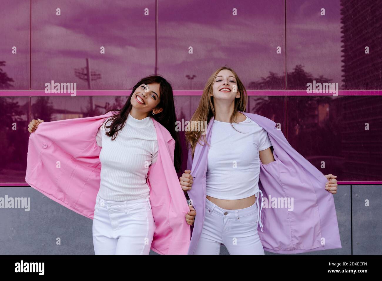 Belle sorelle che indossano giacca in piedi contro parete di vetro acrilico Foto Stock