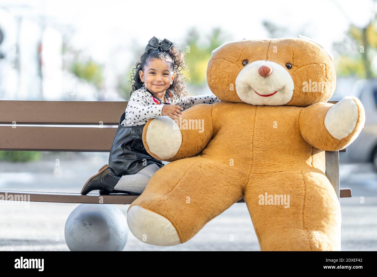 Ragazza sorridente seduta con orsacchiotto sulla panchina Foto Stock