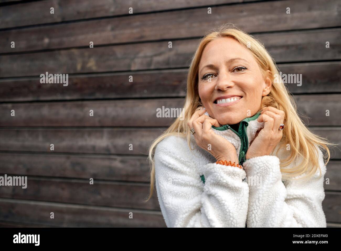Donna che indossa abiti caldi sorridendo mentre si trova contro il muro di legno Foto Stock