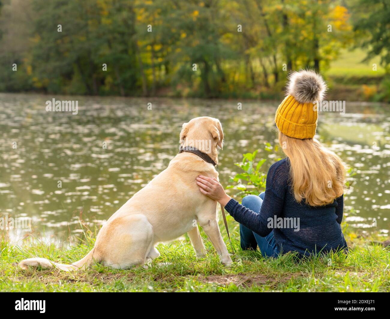 Donna bionda seduta con il cane a Lakeshore durante l'autunno Foto Stock