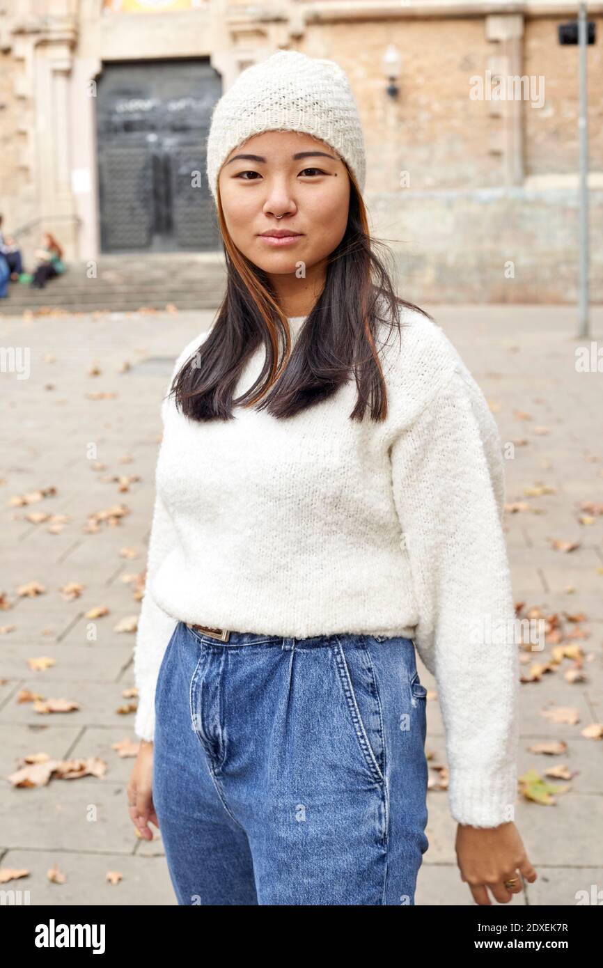 Giovane donna che indossa un cappello a maglia in piedi sulla strada in città Foto Stock