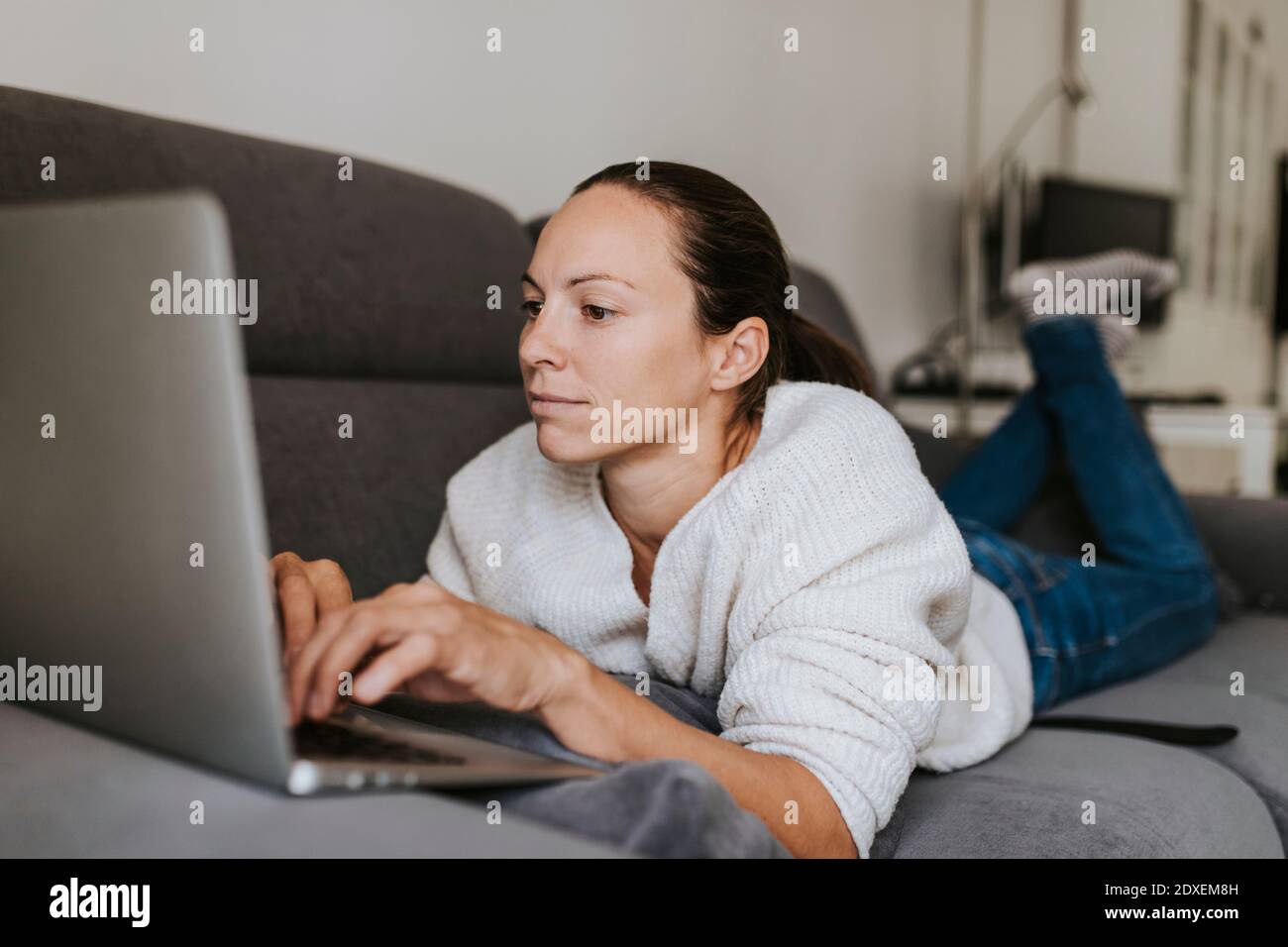 Donna caucasica che usa il computer portatile mentre si sdraia sul divano Foto Stock