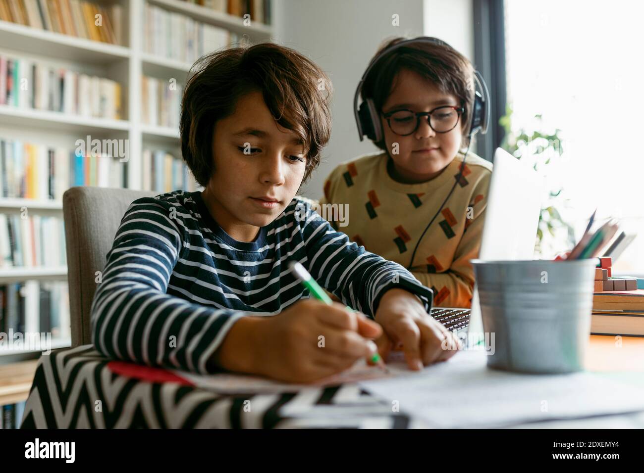 Ragazzo che scrive note mentre l'amico maschio è seduto accanto a lui casa Foto Stock