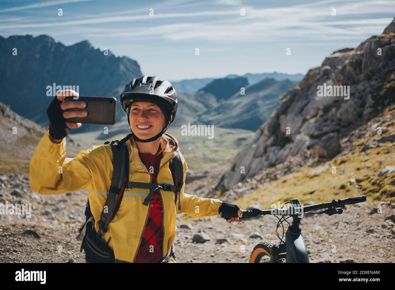 Sorridente ciclista femminile che prende selfie con mountain bike contro la montagna, Parco Nazionale Picos de Europa, Cantabria, Spagna Foto Stock