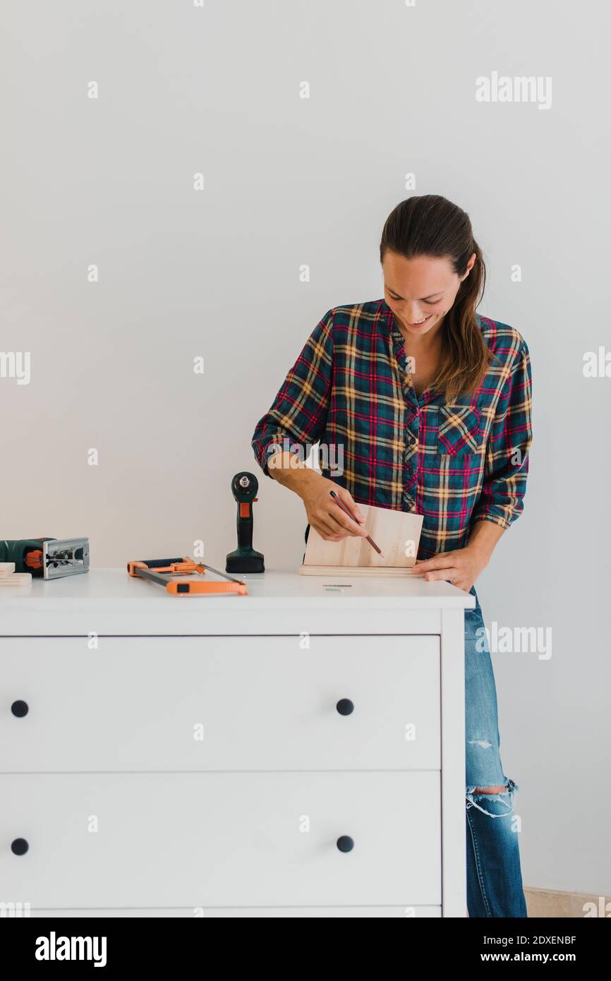 Donna mid adulta che contrassegna sul legno mentre fa il lavoro fai da te a casa Foto Stock