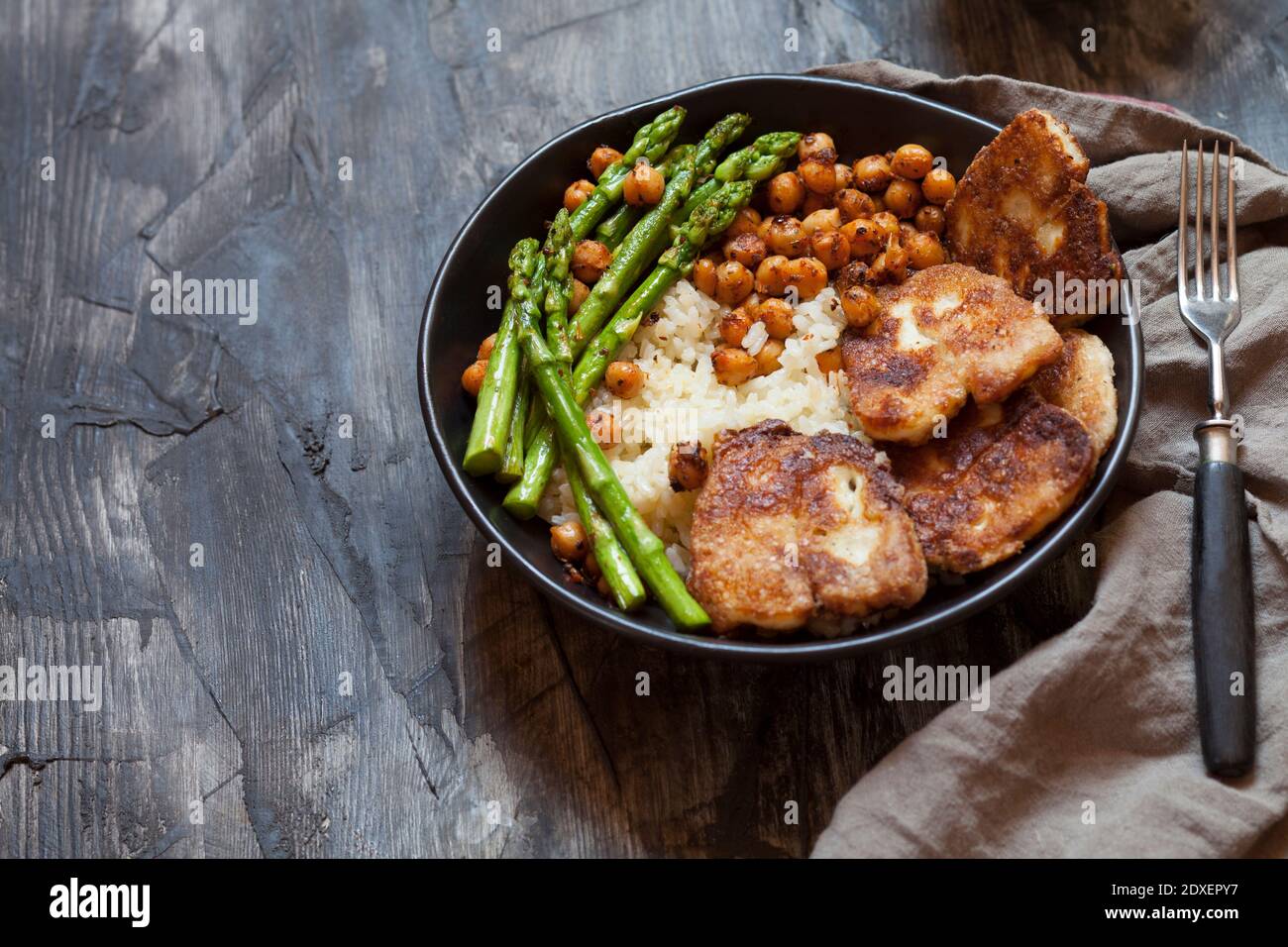 Ciotola di riso con ceci, gambi di asparagi e formaggio halloumi fritto Foto Stock