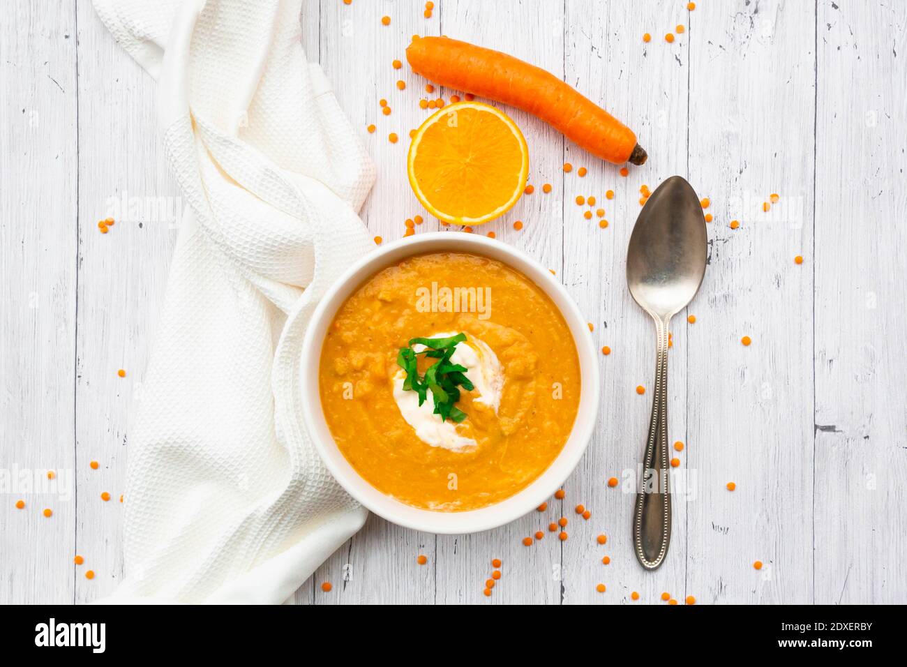 Ciotola di zuppa di lenticchie vegetariane con carote, succo d'arancia, crema fraiche e prezzemolo Foto Stock