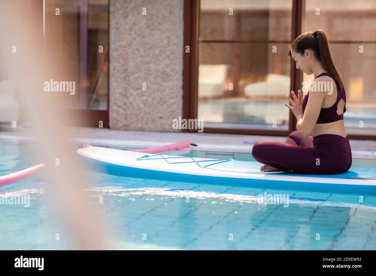 Istruttore femminile che pratica yoga su paddleboard sopra la piscina Foto Stock