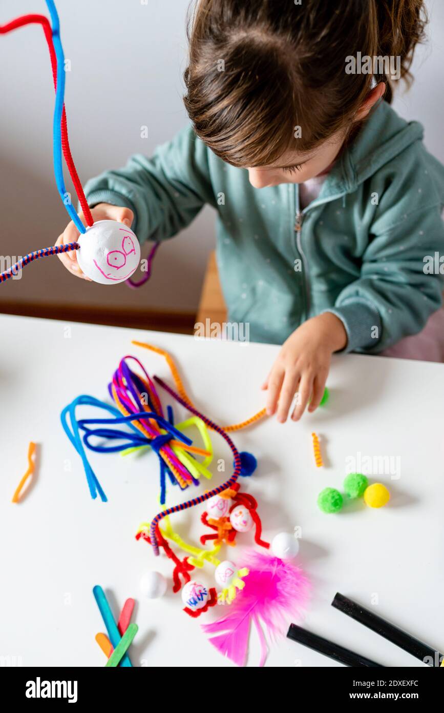 Bambina che gioca con pulitore tubo e palla di stirofoam su tavolo a casa Foto Stock