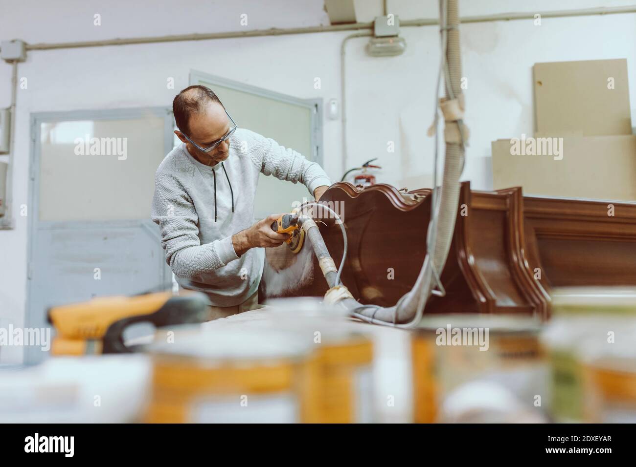 Operatore manuale che utilizza la levigatrice sui mobili durante il lavoro in officina Foto Stock
