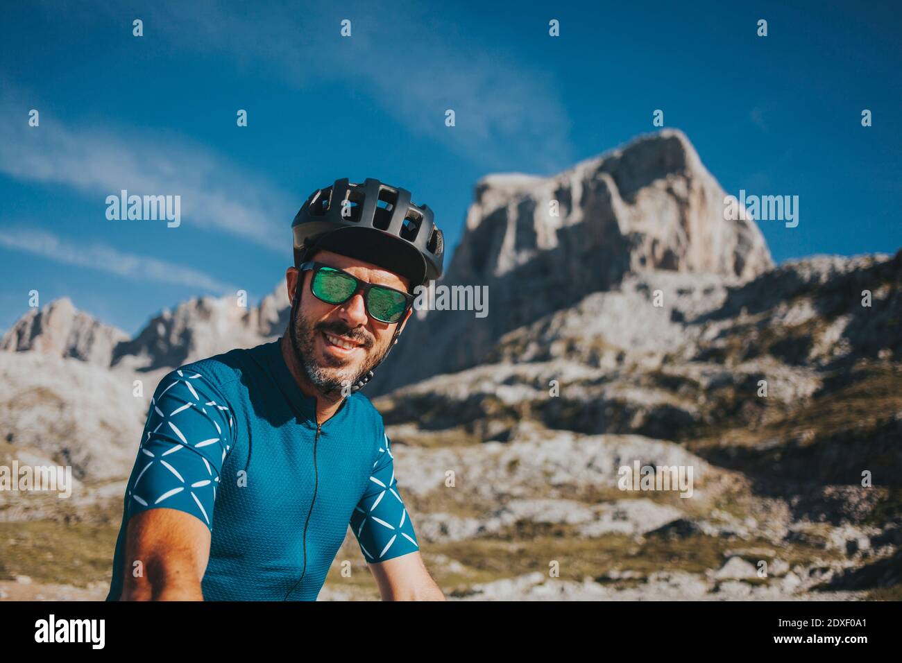 Sorridente ciclista maschile per adulti di media taglia con casco da bicicletta e occhiali da sole al Parco Nazionale Picos de Europa, Cantabria, Spagna Foto Stock