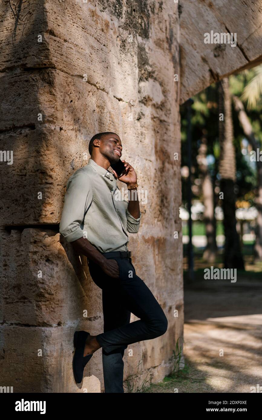 Imprenditore maschile che parla su smartphone con la mano in tasca al parco Foto Stock