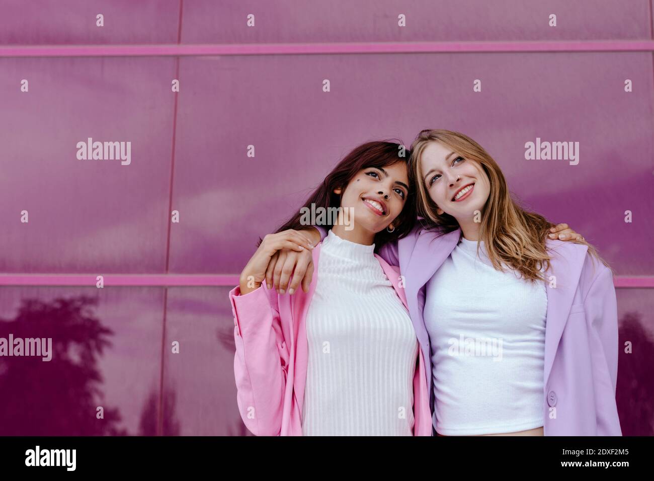 Sorelle premurose con braccia intorno contro parete di vetro acrilico Foto Stock