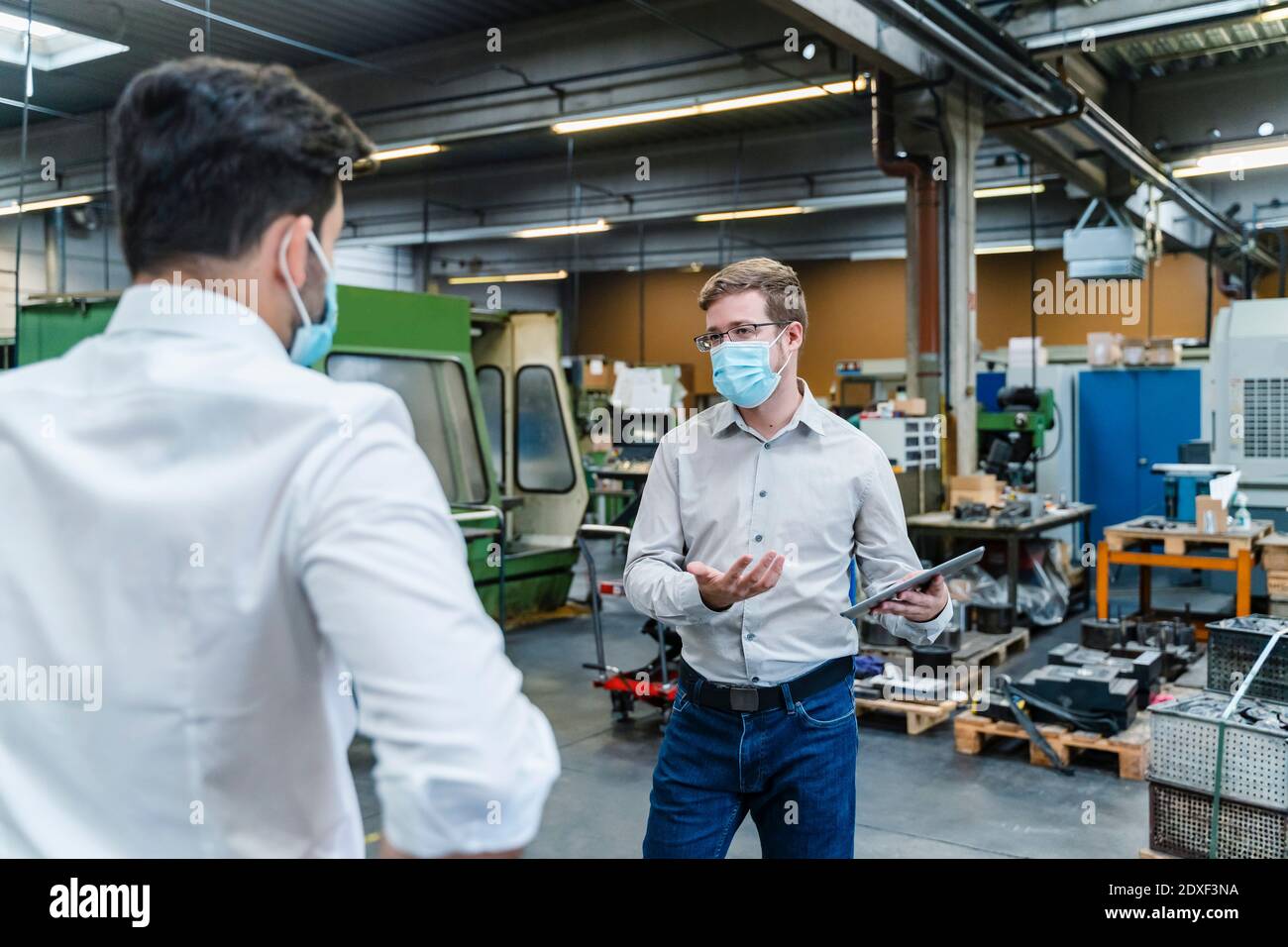 Gli imprenditori maschili discutono mentre indossano la maschera protettiva del viso nell'industria Foto Stock